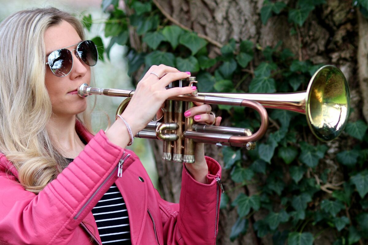 Jem Andrews playing trumpet outdoors in a pink jacket